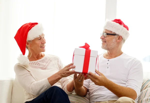 Felice coppia di anziani in cappelli di Babbo Natale con scatola regalo — Foto Stock