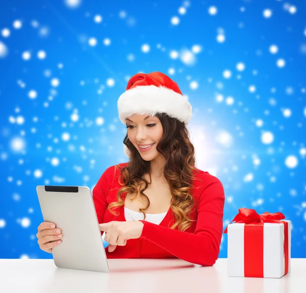 Femme souriante en santa chapeau avec cadeau et tablette pc — Photo