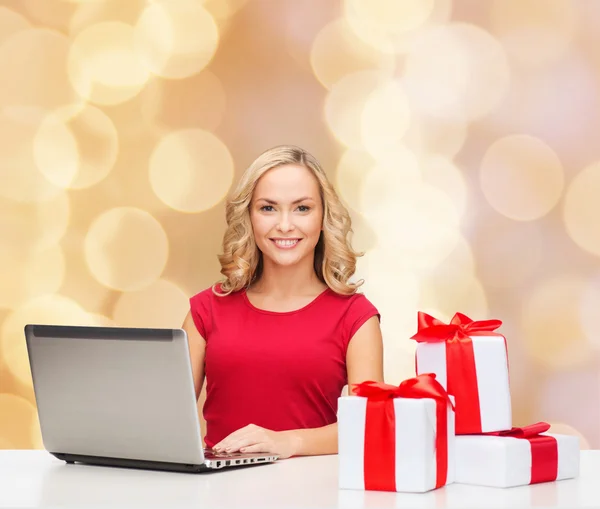 Femme souriante en chemise rouge avec cadeaux et ordinateur portable — Photo