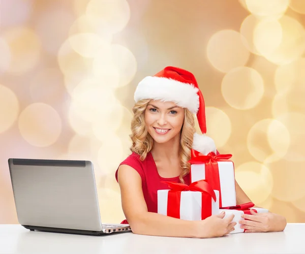 Smiling woman in santa hat with gifts and laptop — Stock Photo, Image