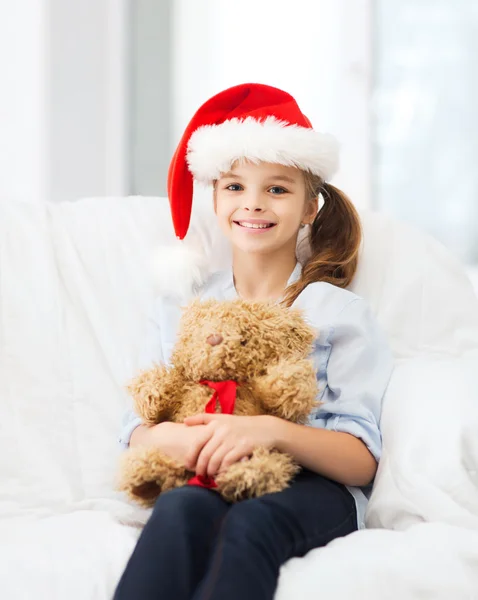 Oyuncak ayı ile santa yardımcı şapkalı kız gülümseyerek — Stok fotoğraf