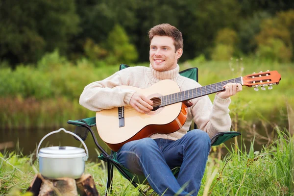 Χαμογελαστός άνθρωπος με κιθάρα και dixie στο κάμπινγκ — Φωτογραφία Αρχείου