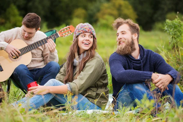 Groep lachende vrienden met gitaar buitenshuis — Stockfoto