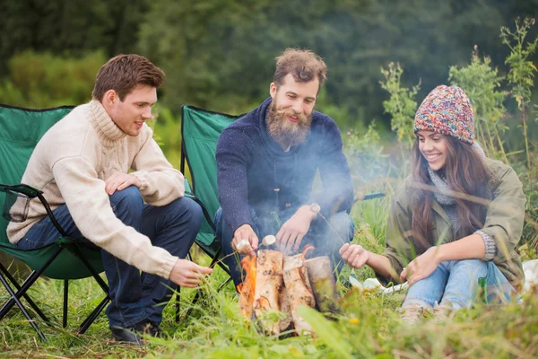 Group of smiling friends sitting around bonfire — Stock Photo, Image