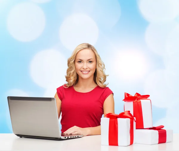 Smiling woman in red shirt with gifts and laptop — Stock Photo, Image