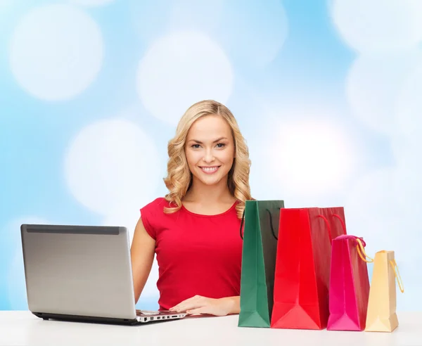 Mulher sorridente em vestido vermelho com presentes e laptop — Fotografia de Stock