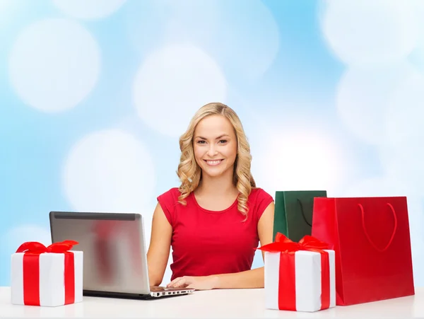 Mulher sorridente em camisa vermelha com presentes e laptop — Fotografia de Stock