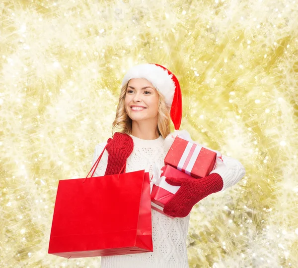 Souriant jeune femme dans santa chapeau d'aide avec des cadeaux — Photo