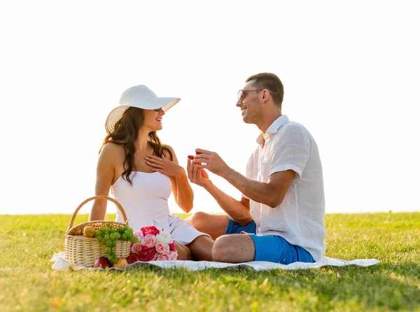 Sonriente pareja con pequeña caja de regalo roja en el picnic —  Fotos de Stock