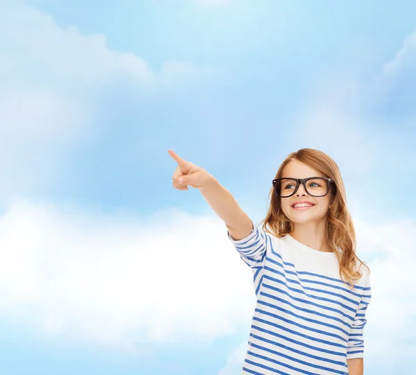 Cute little girl in eyeglasses pointing in the air — Stock Photo, Image