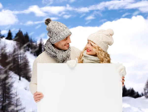 Lächelndes Paar in Winterkleidung mit weißem Brett — Stockfoto