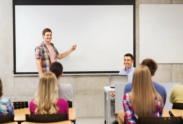 Grupp studenter och leende lärare i klassrummet — Stockfoto