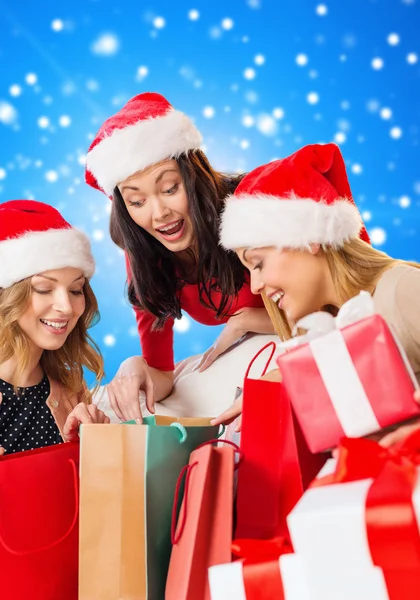 Souriantes jeunes femmes dans des chapeaux de Père Noël avec des cadeaux — Photo