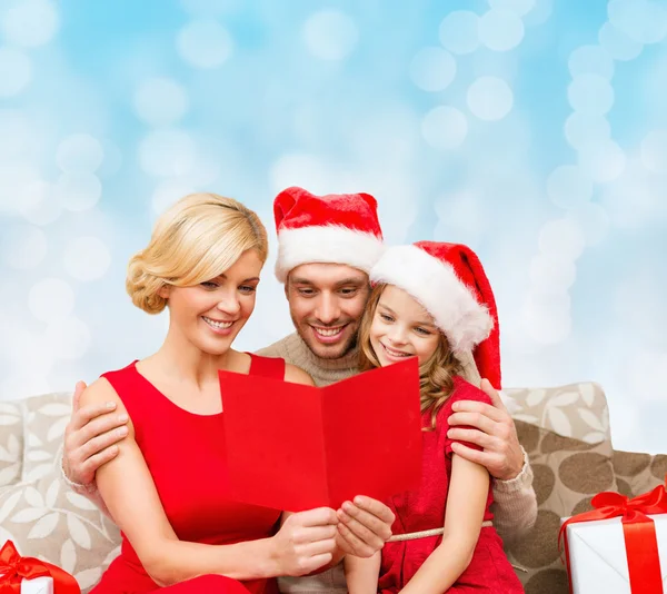 Famiglia felice in cappelli di Babbo Natale con biglietto di auguri — Foto Stock