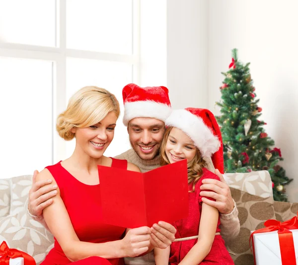 Famiglia felice in cappelli di Babbo Natale con biglietto di auguri — Foto Stock