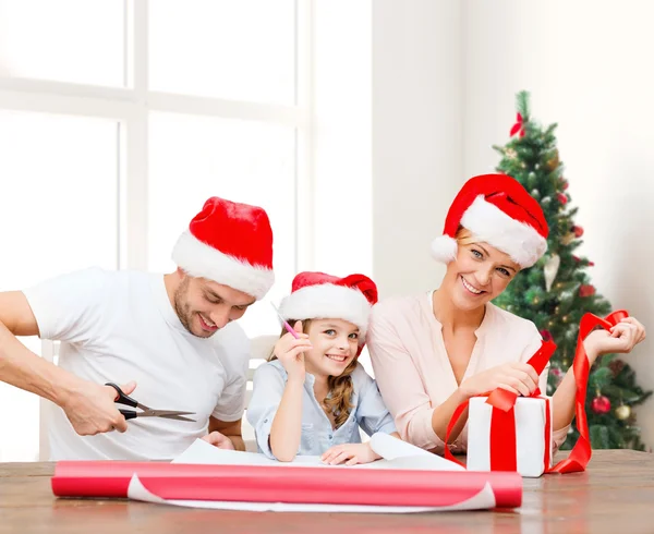 Happy family in santa helper hats packing gift — Stock Photo, Image