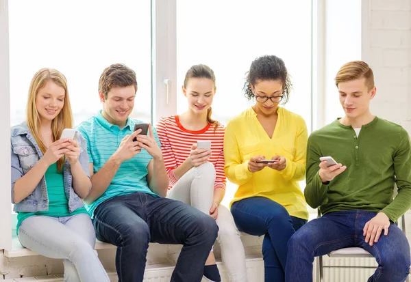 Estudiantes sonrientes con mensajes de texto de teléfonos inteligentes en la escuela — Foto de Stock