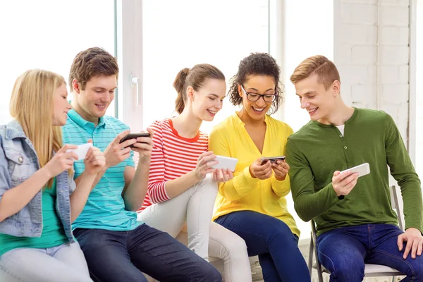 Smiling students with smartphone texting at school — Stock Photo, Image