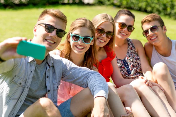 面带微笑的朋友用智能手机坐在草地上 — 图库照片