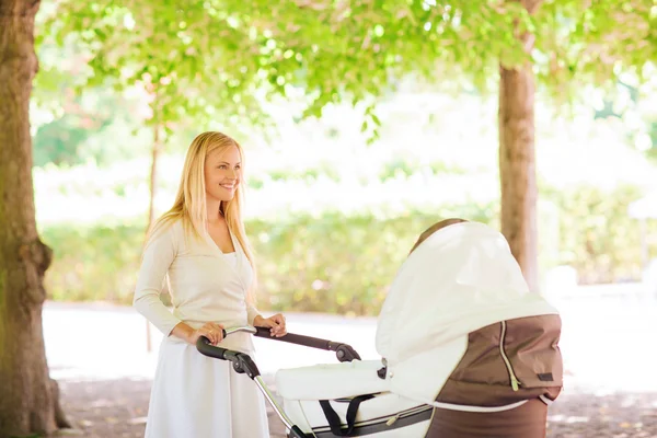 Gelukkig moeder met wandelwagen in park — Stockfoto