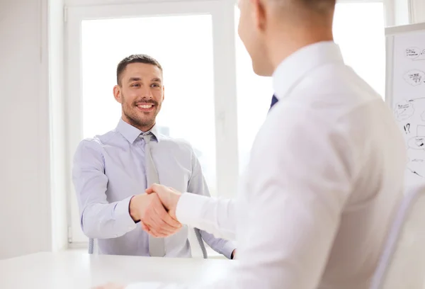 Двоє усміхнених бізнесменів тремтять руками в офісі Стокове Зображення