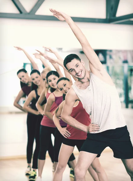 Grupo de personas sonrientes estirándose en el gimnasio — Foto de Stock