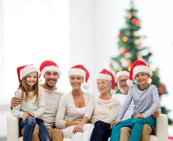 Szczęśliwą rodzinę w santa kapelusze pomocnika, siedząc na kanapie — Zdjęcie stockowe