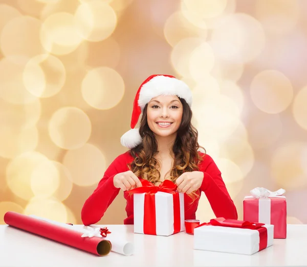 Sorrindo mulher em santa helper chapéu embalagem presentes — Fotografia de Stock