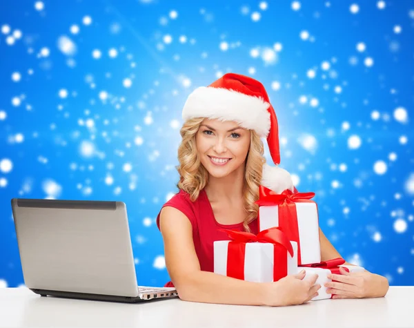 Lachende vrouw in Kerstman hoed met giften en laptop — Stockfoto