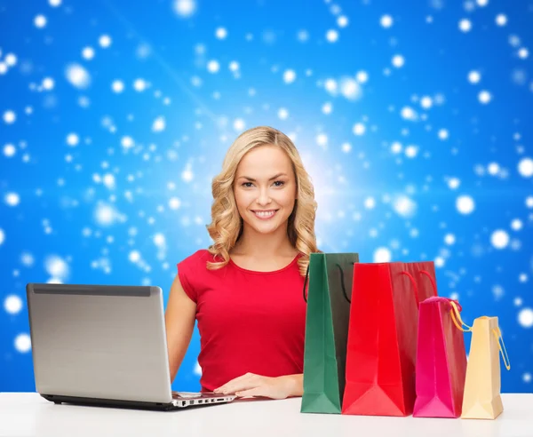 Femme souriante en robe rouge avec des cadeaux et ordinateur portable — Photo