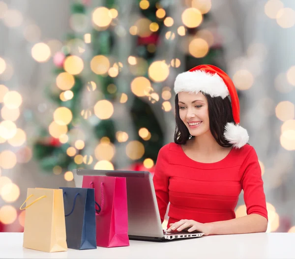 Donna sorridente in cappello di Babbo Natale con borse e laptop — Foto Stock