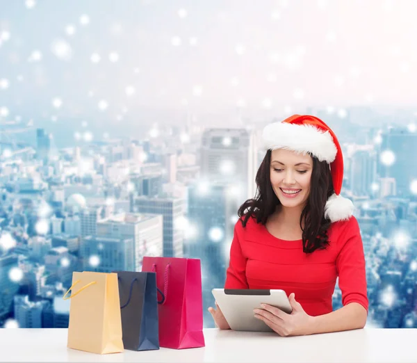 Donna sorridente in cappello di Babbo Natale con borse e tablet pc — Foto Stock