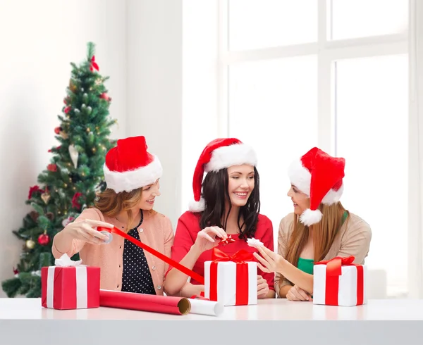 Sonrientes mujeres en santa helper sombreros embalaje regalos — Foto de Stock