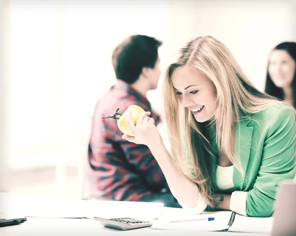 Hymyilevä opiskelija tyttö syö omenaa koulussa — kuvapankkivalokuva