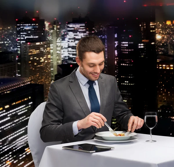 Hombre sonriente con la tableta PC comer plato principal —  Fotos de Stock