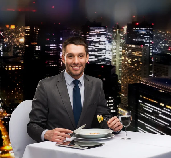 Hombre sonriente con la tableta PC comer plato principal —  Fotos de Stock