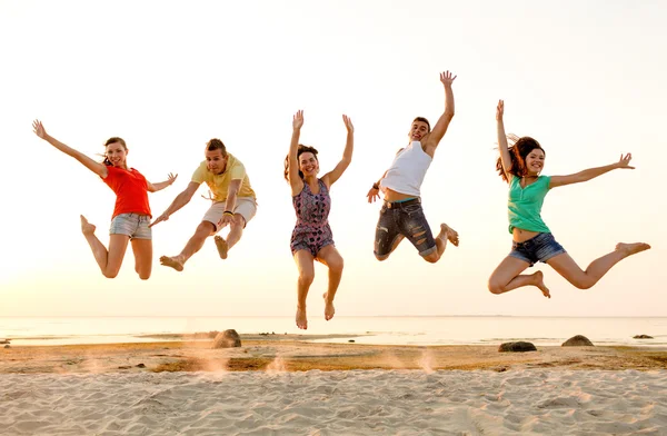 Lächelnde Freunde tanzen und springen am Strand — Stockfoto