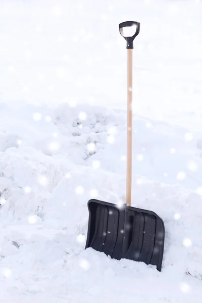 Black snowshowel with wooden handle in snow pile — Stock Photo, Image