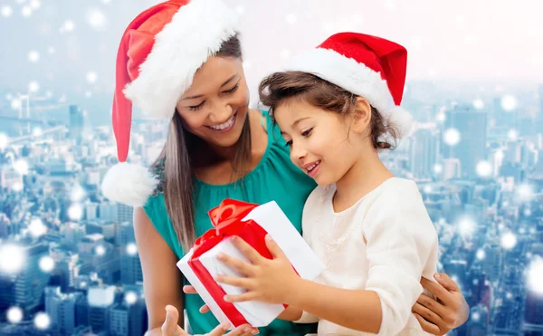 Happy mother and girl in santa hats with gift box — Stock Photo, Image