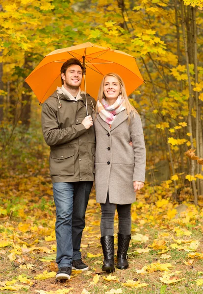 Coppia sorridente con ombrellone nel parco autunnale — Foto Stock