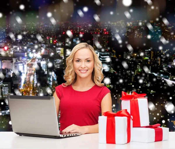 Donna sorridente in camicia rossa con regali e laptop — Foto Stock