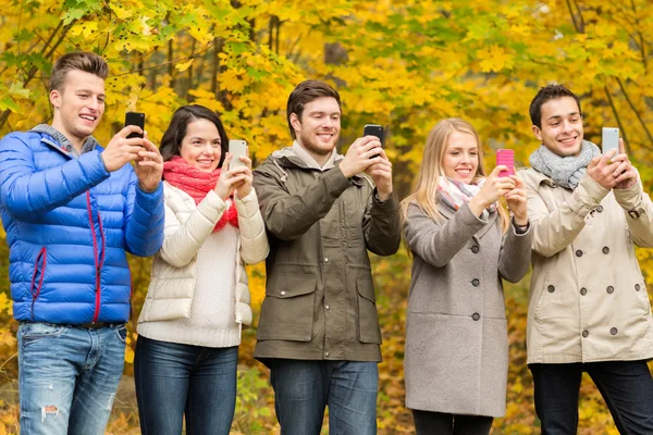 Улыбающиеся друзья со смартфонами в городском парке — стоковое фото