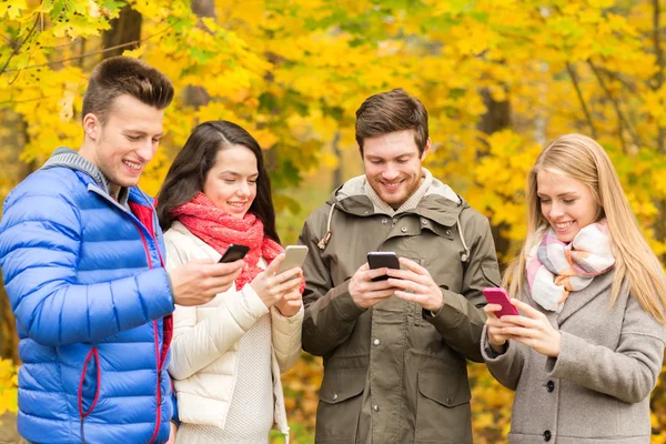 Amigos sonrientes con teléfonos inteligentes en el parque de la ciudad —  Fotos de Stock