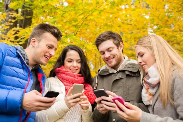 Amigos sonrientes con teléfonos inteligentes en el parque de la ciudad — Foto de Stock