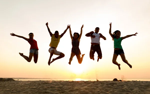 Amigos sonrientes bailando y saltando en la playa — Foto de Stock