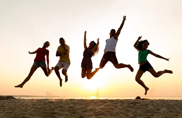 Smiling friends dancing and jumping on beach — Stock Photo, Image