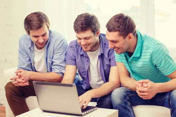 Amici sorridenti con il computer portatile a casa — Foto Stock