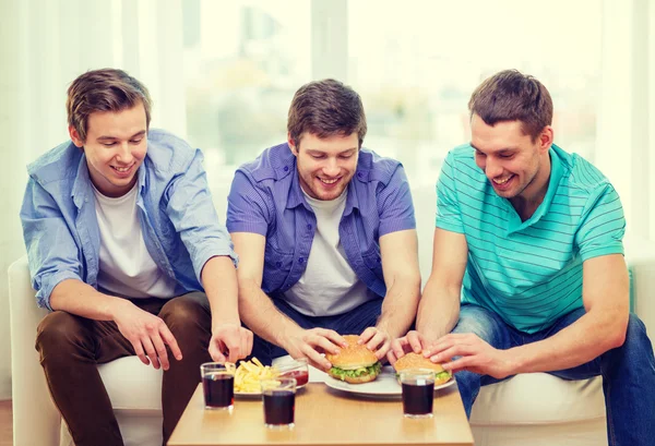 Lachende vrienden met soda en hamburgers thuis — Stockfoto