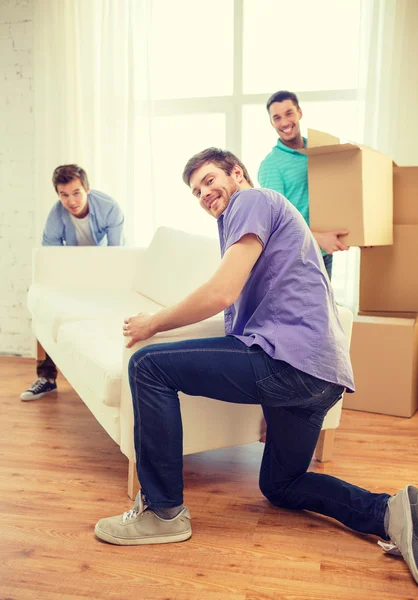 Smiling friends with sofa and boxes at new home — Stock Photo, Image