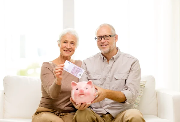 Seniorenpaar mit Geld und Sparschwein zu Hause — Stockfoto